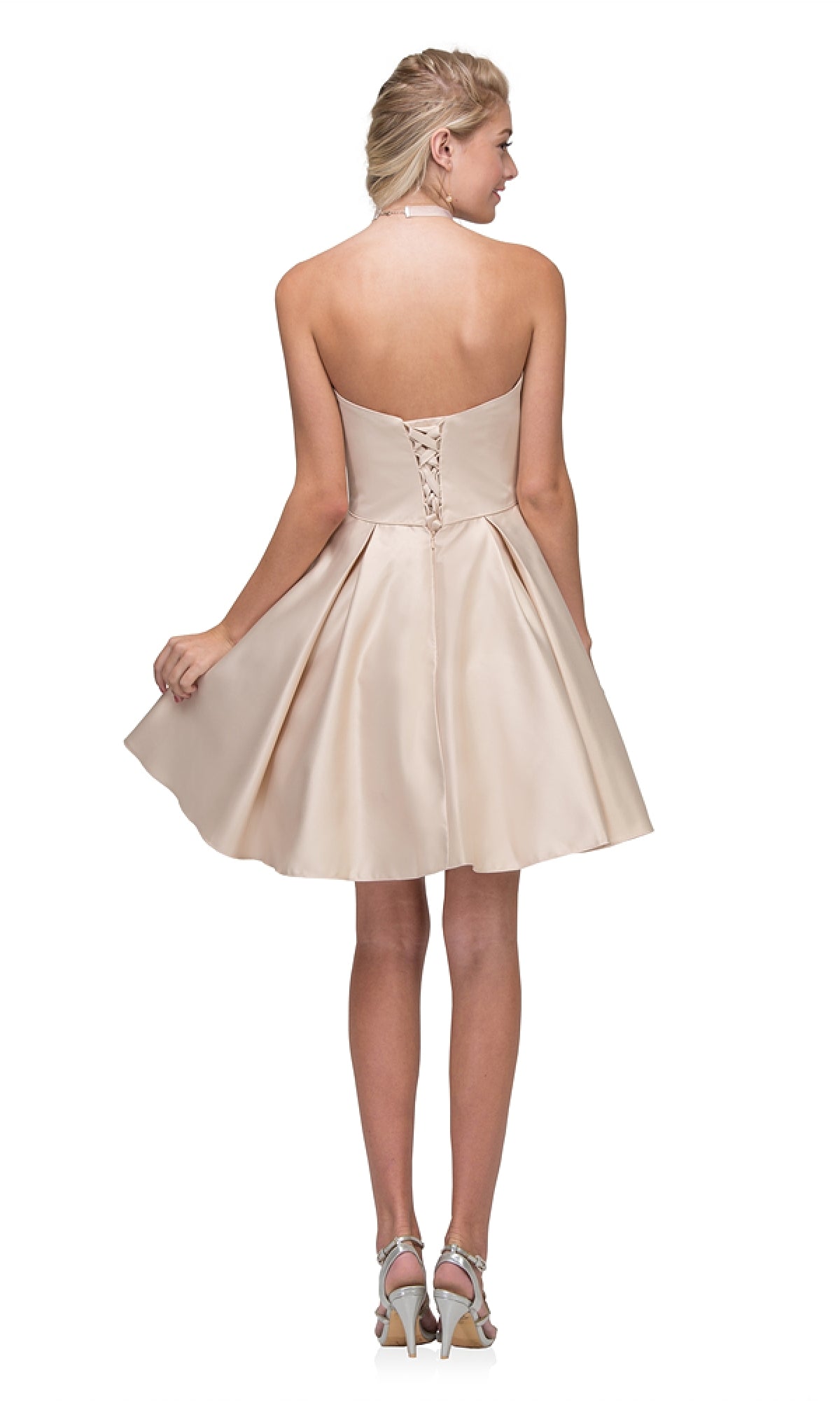 A woman with braided light hair and heeled sandals faces away, wearing the Strapless Short Wedding-Guest Dress: Eureka 6622 in light beige, featuring a lace-up back and holding part of its skirt.
